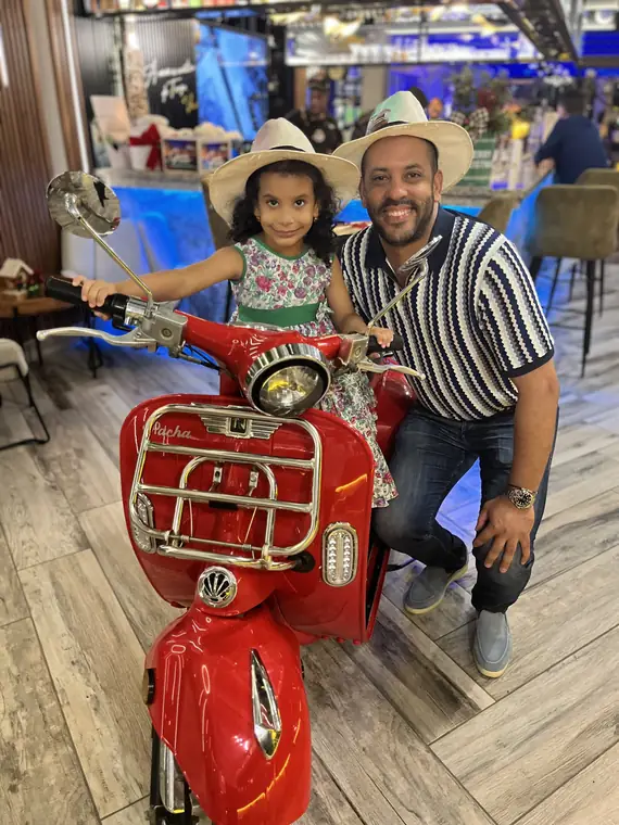 Padre e hija con sombreros en la Vespa roja