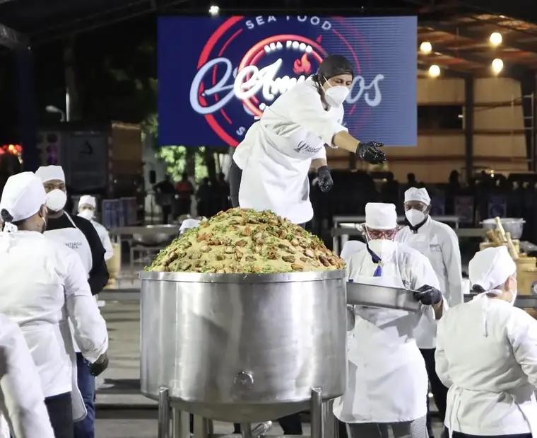 Cocinera sirviendo el mofongo gigante frente a la pantalla con el logo de Amigos